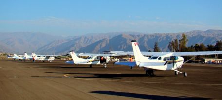 Fleet of small aircraft lined up at Nazca Airport with the Andes Mountains in the background.