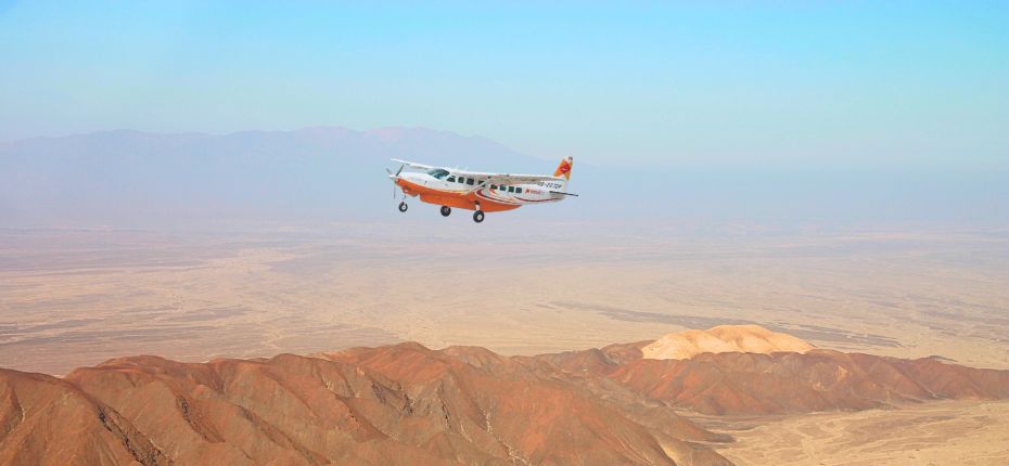 Scenic aerial view of a Cessna Grand Caravan flying above the red desert mountains of Nazca