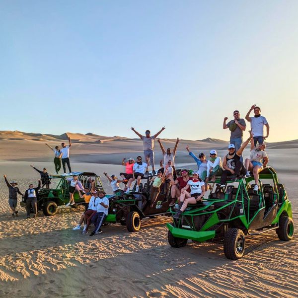 Excited travelers posing beside dune buggies in the desert.