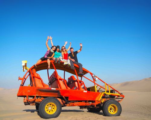 Group of friends cheering on top of a red dune buggy in the desert.