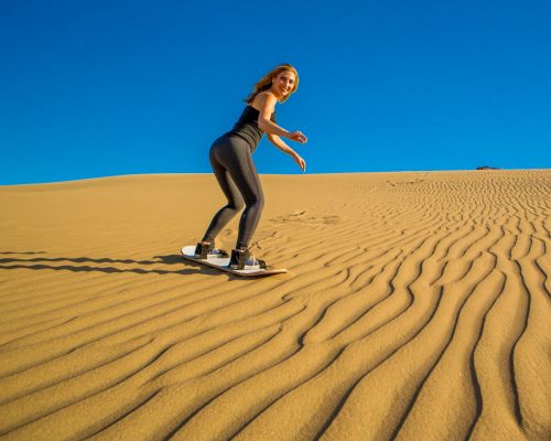Woman riding a sandboard down a golden desert dune.