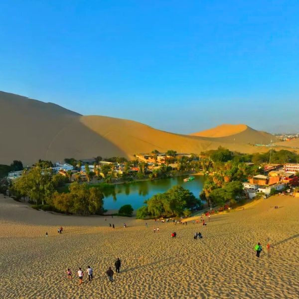 The oasis of Huacachina surrounded by desert dunes at sunset.