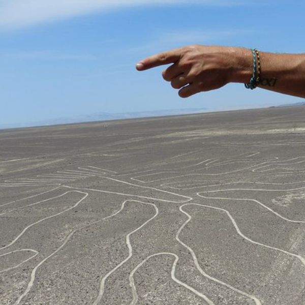Guide pointing toward a Nazca geoglyph in the desert