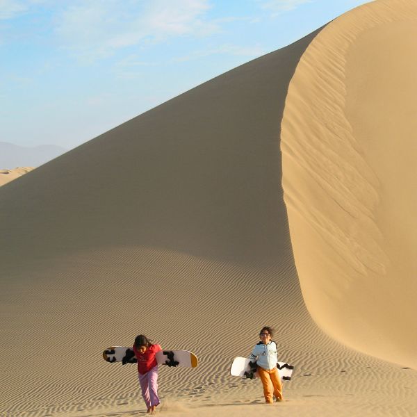Kids sandboarding in giant desert dunes