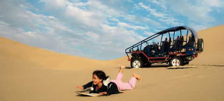 Young explorer sandboarding beside a desert buggy in the Usaka dunes