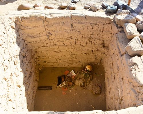 Pre-Inca mummy with burial goods inside a rectangular tomb.
