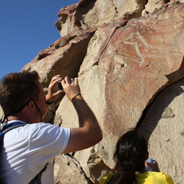 Tourists examining a horse-like figure carved on a stone cliff.