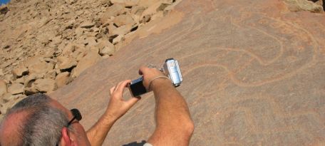 Traveler photographing a snake petroglyph engraved on a stone surface.